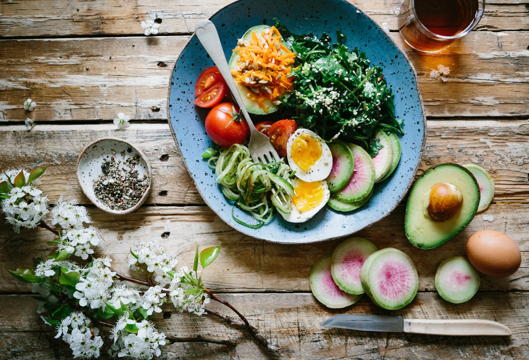 A bowl of greens, eggs, tomatoes and avocado on a wooden table